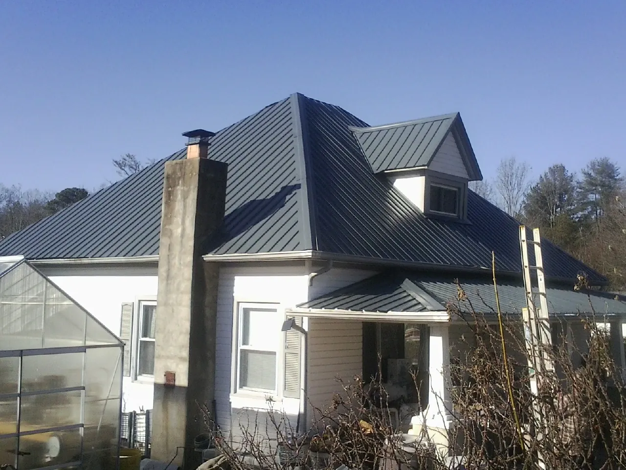 Dark blue standing seam metal roof on a white farmhouse with dormer — Slate & Tile Roof Repair by Roofing Brothers in Neosho