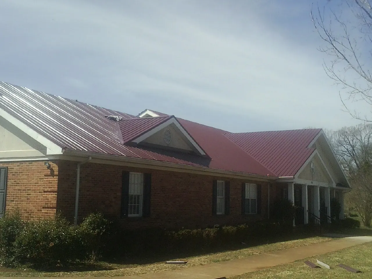 Red metal roof with gabled entries on a long brick building, from a Hail Damage Roof Repair job in Neosho