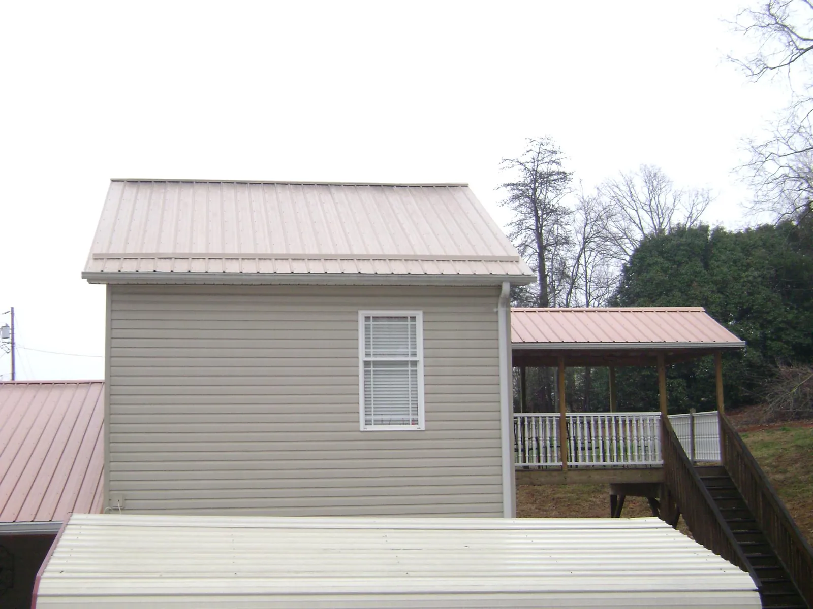 Tan metal roofs on a two story addition and attached porch, from a Roof Replacement job in Neosho